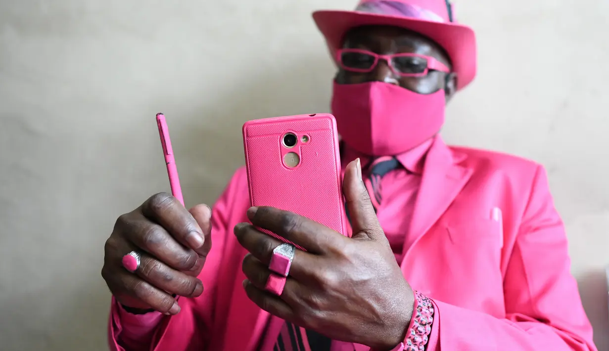 Fashionista Kenya, James Mwangi Maina bermain ponsel sambil memamerkan setelan jasnya yang senada dengan pakaian dan aksesorisnya, termasuk masker di Nairobi, 5 Agustus 2020. Mwangi memiliki lebih dari 160 jas yang warnanya serasi dengan aksesoris yang dimilikinya. (Simon MAINA/AFP)