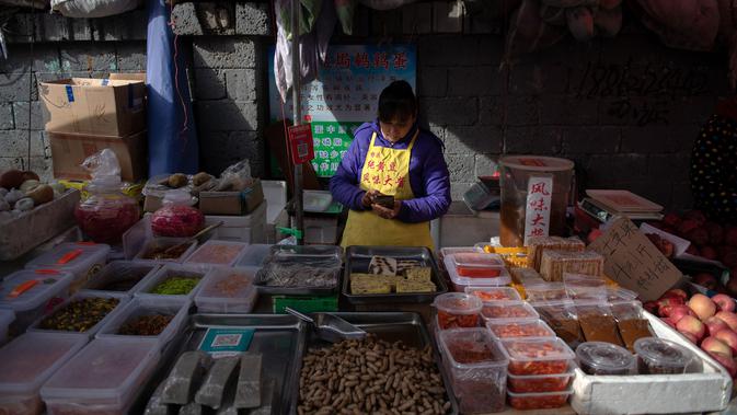 Seorang pedagang melihat ponsel miliknya di pasar di Beijing (20/11). (AFP Photo/Nicolas Asfouri)