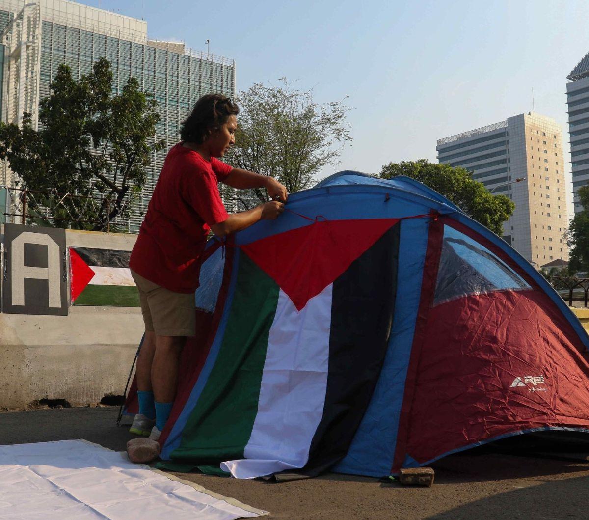Seorang pengunjuk rasa yang tergabung dalam Koalisi Musisi untuk Gaza memasang bendera Palestina pada tenda yang didirikan di depan Kedutaan Besar Amerika Serikat (AS), Jakarta, Jumat (10/5/2024). Menyusul gerakan mahasiswa di sejumlah kampus di Amerika S