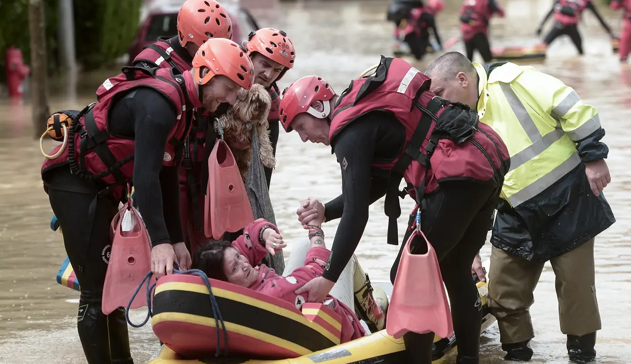 Seorang wanita dibantu oleh petugas pemadam kebakaran ke perahu kecil setelah hujan lebat di Salies-de-Bearn, Perancis barat daya (13/6). (AFP Photo/Iroz Gaizka)