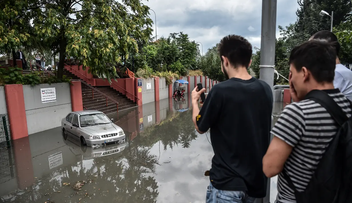 Seorang pria mengambil gambar sebuah mobil yang terendam akibat tingginya debit air banjir di kota Istanbul, Turki, Selasa (18/7). Sejumlah besar wilayah kota terendam banjir cukup parah akibat diguyur hujan lebat selama 12 jam. (OZAN KOSE / AFP)