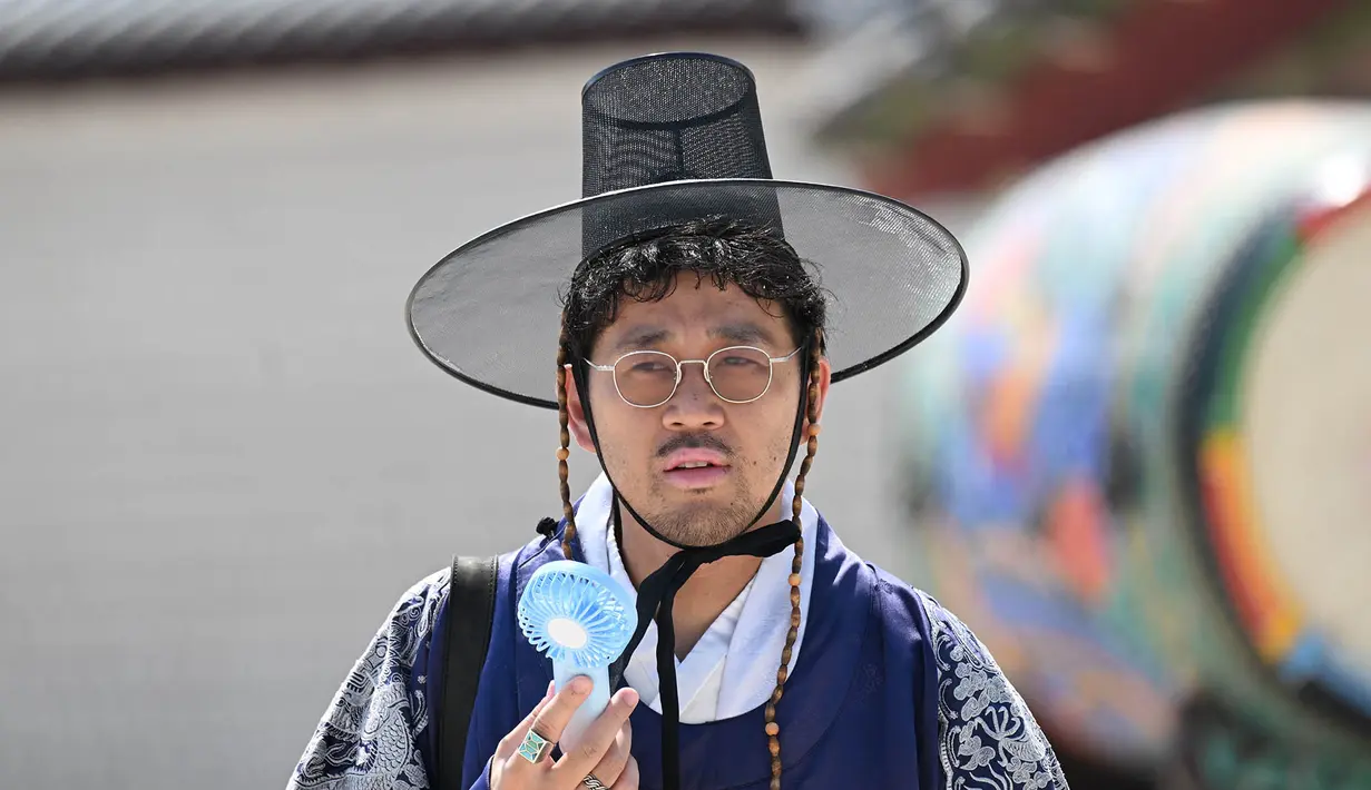 Seorang turis yang mengenakan pakaian tradisional Hanbok menggunakan kipas portabel untuk mendinginkan diri di Istana Gyeongbokgung di Seoul, Korea Selatan, Senin,  3 Agustus 2026. (AFP/  Jung Yeon-je)