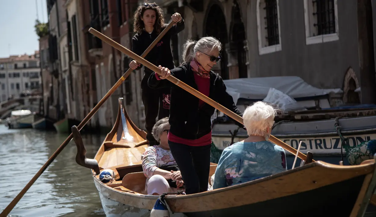 Elena Almansi (tengah), anggota Row Venice, mengajarkan mendayung gondola bagi wisatawan di sebuah kanal di Venesia, Italia pada 16 Mei 2019. Pengalaman ini bisa dimiliki dengan sekitar Rp 1,37 juta per gondola selama 90 menit untuk empat orang yang dimulai pukul 10.00 pagi. (MARCO BERTORELLO/AFP)