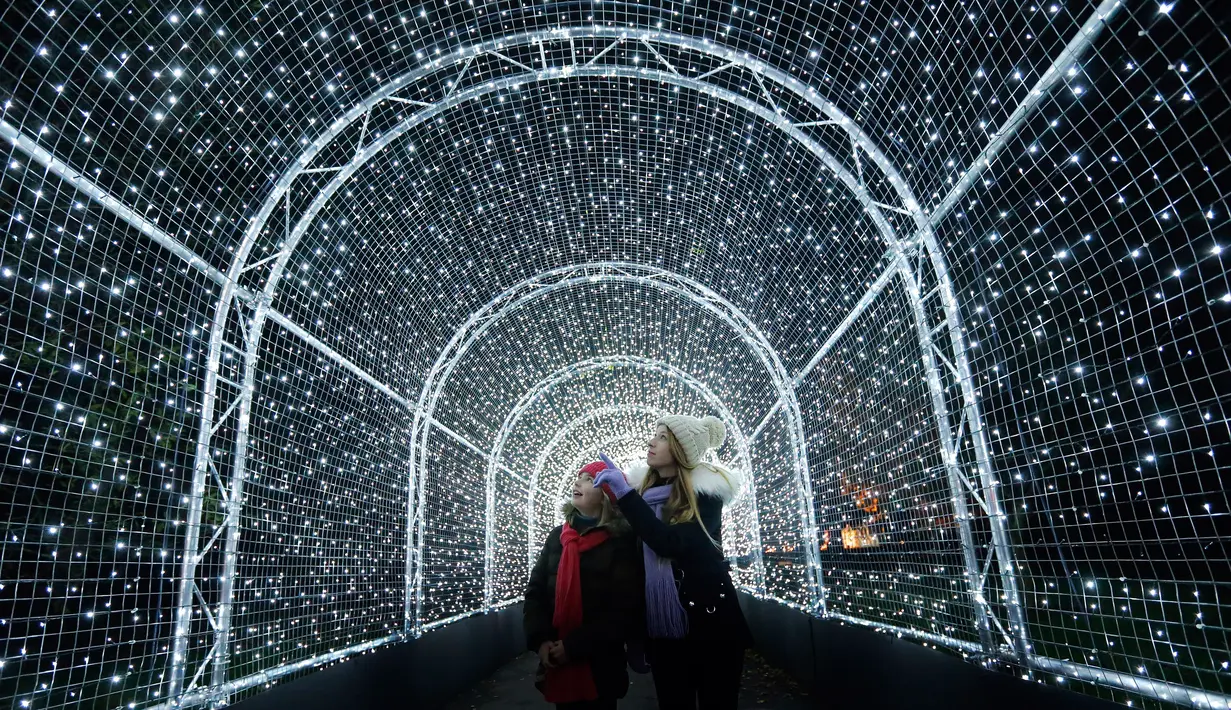 Pengunjung berjalan melewati terowongan yang dipenuhi cahaya lampu di Kew Gardens, London (21/11). Jelang perayaan Natal, Kew Gardens atau The Royal Botanical Garden dihiasi seni intalasi cahaya. (AP Photo/Frank Augstein)