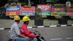 Pengendara melintas di depan karangan bunga berisi dukungan pada KPK di Gedung KPK, Jakarta, Senin (20/11). Karangan bunga tersebut sebagai bentuk dukungan masyarakat kepada KPK terhadap pemberantasan kasus korupsi e-KTP. (Liputan6.com/Faizal Fanani)