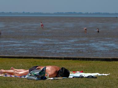 Seorang pria berjemur saat suhu mencapai 34 derajat Celcius di dekat pantai Laut Utara di Wremen, Jerman barat (24/7/2019). Peramal cuaca memprediksi suhu tertinggi di seluruh Eropa barat yang terkena gelombang panas akan mencetak rekor suhu terbaru.  (AFP Photo/Patrik Stollarz)