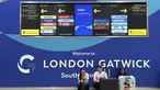Para penumpang duduk di depan papan informasi yang menunjukkan lokasi meja maskapai di Bandara Gatwick dekat London, Inggris, Kamis 12 Juni 2025. (AP/Kin Cheung)