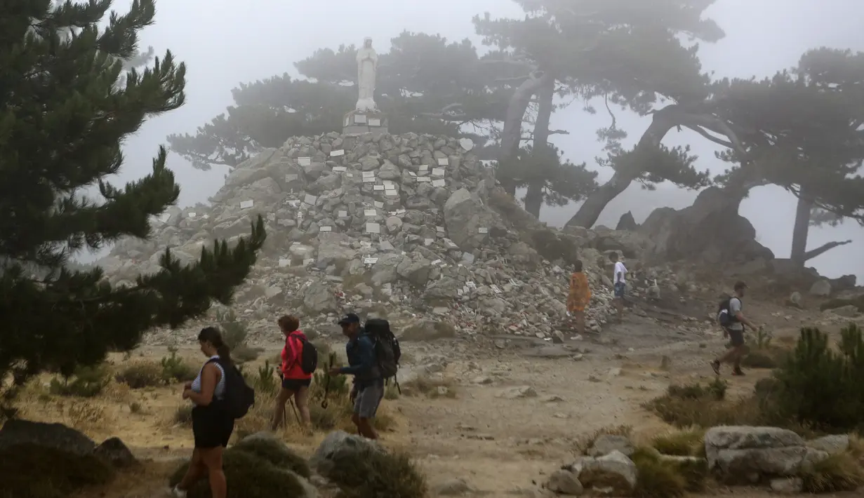 Sejumlah wisatawan berjalan di depan patung Notre Dame des Neiges di hutan Bavella, Prancis, Rabu (25/8/2021). Situs wisata alam Bavella dipenuhi oleh pengunjung selama musim panas. (AFP/Pascal Pochard-Casabianca)