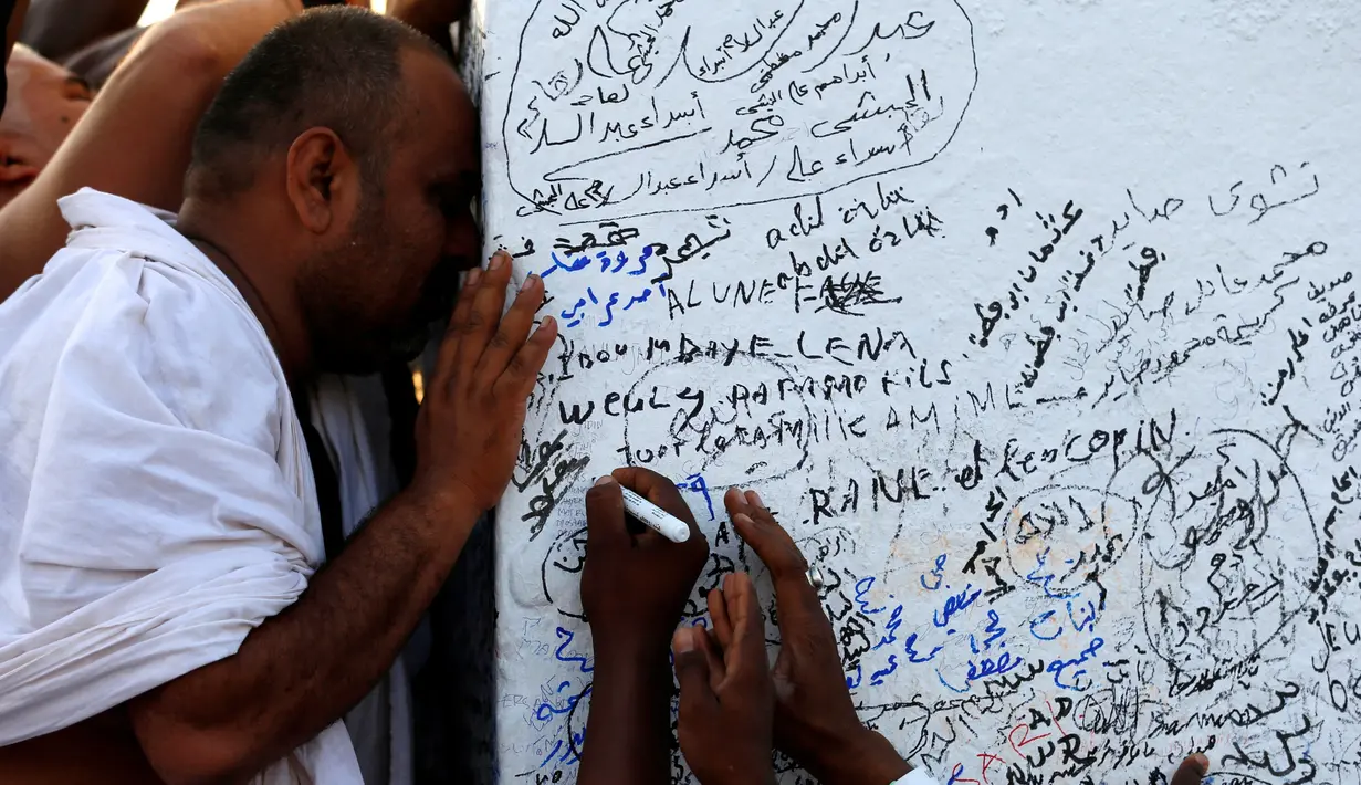 Seorang jemaah terlihat berdoa sementara jemaah lainnya sengaja menuliskan sesuatu di puncak Jabal Rahmah, Arafah, Mekah, Minggu (11/9).  Bukit yang dikenal sebagai Bukit Kasih Sayang itu menjadi pusat prosesi ibadah haji, wukuf. (REUTERS/Ahmed Jadallah)