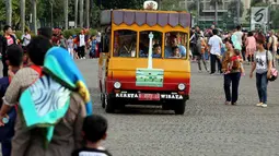 Sejumlah pengunjung menaiki kereta wisata di halaman Monumen Nasional, Jakarta, Rabu (27/6). Libur ketiga Lebaran dimanfaatkan warga untuk bekunjung ke lokasi wisata bersama keluarga. (Liputan6.com/Johan Tallo)