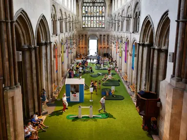Orang-orang bermain di lapangan golf kecil yang didirikan  di dalam Katedral Rochester, Inggris pada 6 Agustus 2019. Lapangan golf ini membentang di sepanjang lorong dan memiliki sembilan lubang dengan miniatur jembatan.  (Ben STANSALL / AFP)