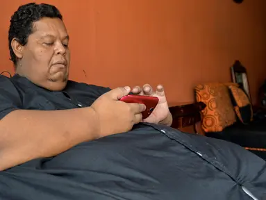 Oscar Vasquez Morales (44) memeriksa ponselnya di Palmira, Kolombia, 19 Maret 2016. Setelah selama berpuluh tahun mengonsumsi junk food, berat badan Oscar melonjak hingga 400 kilogram. (AFP PHOTO/Luis ROBAYO)