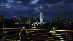 Seorang wanita mengambil gambar cincin Olimpiade yang dipasang di tongkang yang mengapung di air dekat replika Patung Liberty selama Olimpiade Musim Panas 2020 di Tokyo, Jepang  (29/7/2021). (AP Photo/Jae C. Hong)
