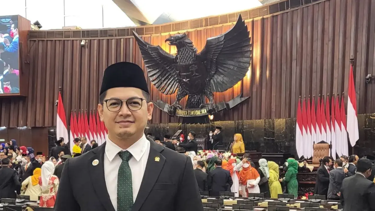 Tommy Kurniawan tampil gagah dengan jas hitam dipadukan dengan kemeja putih serta dasi hijau. Lengkap dengan peci hitamnya, ia berfoto dengan latar belakang meja sidang. (Foto: Instagram/@tommykurniawan)