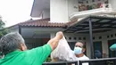 NY (atas) yang sedang melakukan isolasi mandiri karena terjangkit COVID-19 melihat suaminya menerima makanan pemberian warga di kediamannya, Rabu (10/2/2021). Tenaga kesehatan di sebuah RS swasta Jakarta itu dinyatakan positif terinfeksi COVID-19 tanpa gejala (OTG). (Liputan6.com/Herman Zakharia)