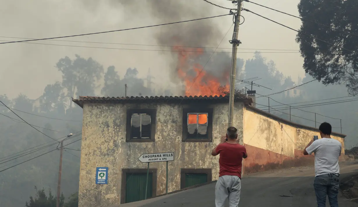 Warga mengambil gambar rumah yang terbakar di Caminho do Meio selama kebakaran hutan yang melanda pulau Madeira di Portugal, Rabu (10/8). Sedikitnya tiga orang tewas dan lebih dari 1.000 orang dievakuasi akibat kebakaran ini. (REUTERS/Duarte Sa)