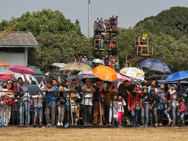 Sejumlah warga mengenakan payung saat menyaksikan perayaan HUT ke-74 TNI di Lanud Halim Perdanakusuma, Jakarta Timur, Sabtu (5/10/2019). Warga rela panas-panasan dan berdesak-desakan untuk menyaksikan perayaan HUT ke-74 TNI. (Liputan6.com/JohanTallo)