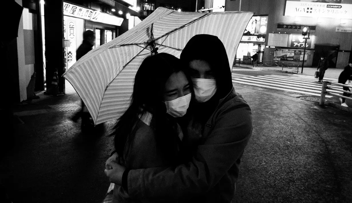 Pasangan berpelukan sambil menunggu di penyeberangan pejalan kaki di Tokyo, (7/3/2020). (AP Photo/Jae C. Hong)
