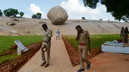 Polisi India berjalan melewati batu 'Krishna's Butter Ball' yang terkenal di Mahabalipuram, Kamis (3/10/2019). Selama 1.300 tahun, batu raksasa seberat 250 ton ini tampak seperti melawan gravitasi. (ARUN SANKAR / AFP)