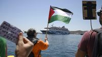 Seorang pengunjuk rasa mengibarkan bendera Palestina saat massa melakukan unjuk rasa di depan kapal pesiar yang membawa turis asal Israel dan berusaha mendekati Pulau Syros di Laut Aegea, Yunani, pada Selasa (22/7/2025). (Dok. Nikos Panagiotopoulos/InTime News via AP)&nbsp;