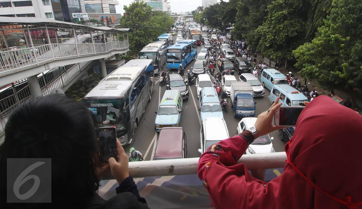 Warga mengabadikan kemacetan yang terjadi di Jalan Salemba Raya, Jakarta, Jumat (2/12). Tingginya mobilisasi massa yang akan mengikuti Aksi 2 Desember mengakibatkan sejumlah ruas jalan menuju Monas macet total. (Liputan6.com/Immanuel Antonius)