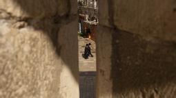 Pria Yahudi Ultra-Ortodoks berjalan di Kota Tua Yerusalem, seperti yang terlihat melalui celah di benteng kuno di Tower of David Museum, Rabu (28/10/2020). Benteng kuno Yerusalem sepi dari turis karena pandemi dan menjalani proyek restorasi dan konservasi besar-besaran. (AP Photo/Maya Alleruzzo)