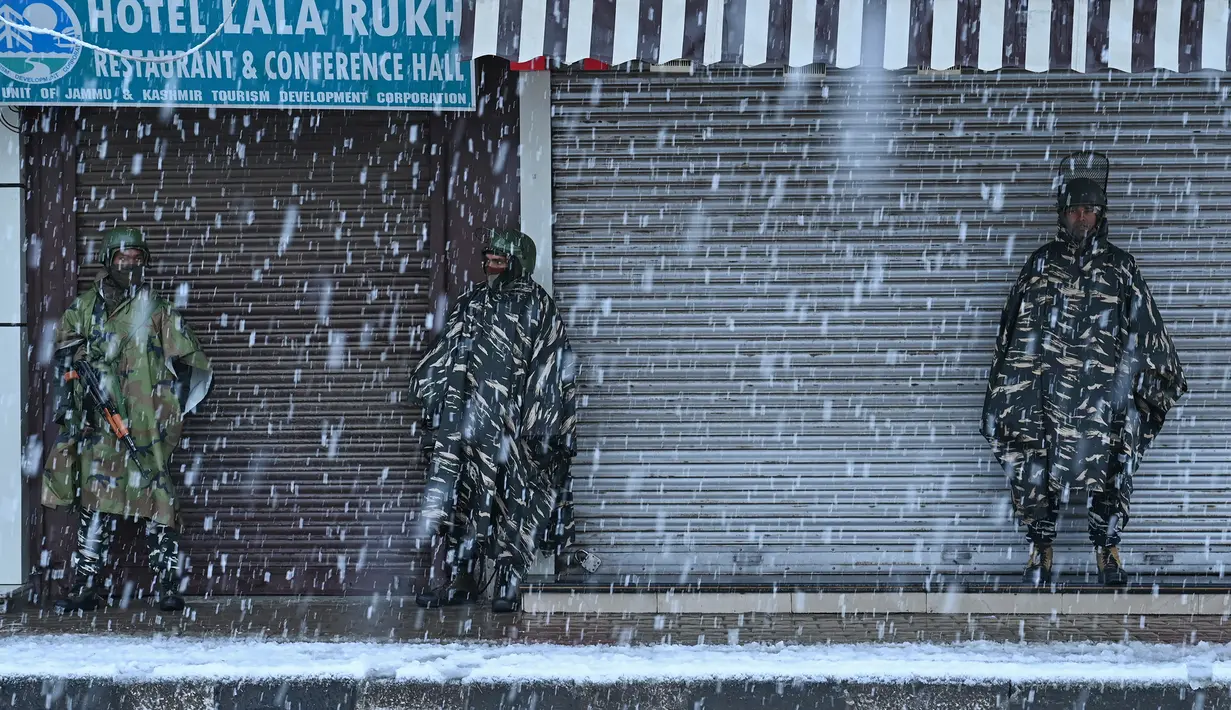 Pasukan paramiliter India berjaga di depan sebuah toko yang tutup saat salju turun di kota utama Kashmir, Srinagar, Kamis (7/11/2019). Srinagar menyambut salju pertama musim ini yang mulai turun. (Photo by Tauseef MUSTAFA / AFP)