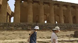 Dua wanita berjalan saat mengunjungi Lembah Kuil selama gelombang panas di dekat Agrigento, Sisilia, Italia (11/8/2021). Gelombang panas yang berkelanjutan akan berlangsung hingga akhir pekan dengan suhu diperkirakan mencapai lebih dari 40 derajat Celcius di banyak bagian dari Italia. (AP Photo/Salv