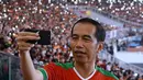 Presiden Joko Widodo (Jokowi) tampak asyik membuat vlog dengan kamera handphone saat menyaksikan laga final Piala Presiden 2018 antara Persija Jakarta vs Bali United di Stadion Utama Gelora Bung Karno, Sabtu (17/2). (Liputan6.com/Pool/Biro Pers Setpres)