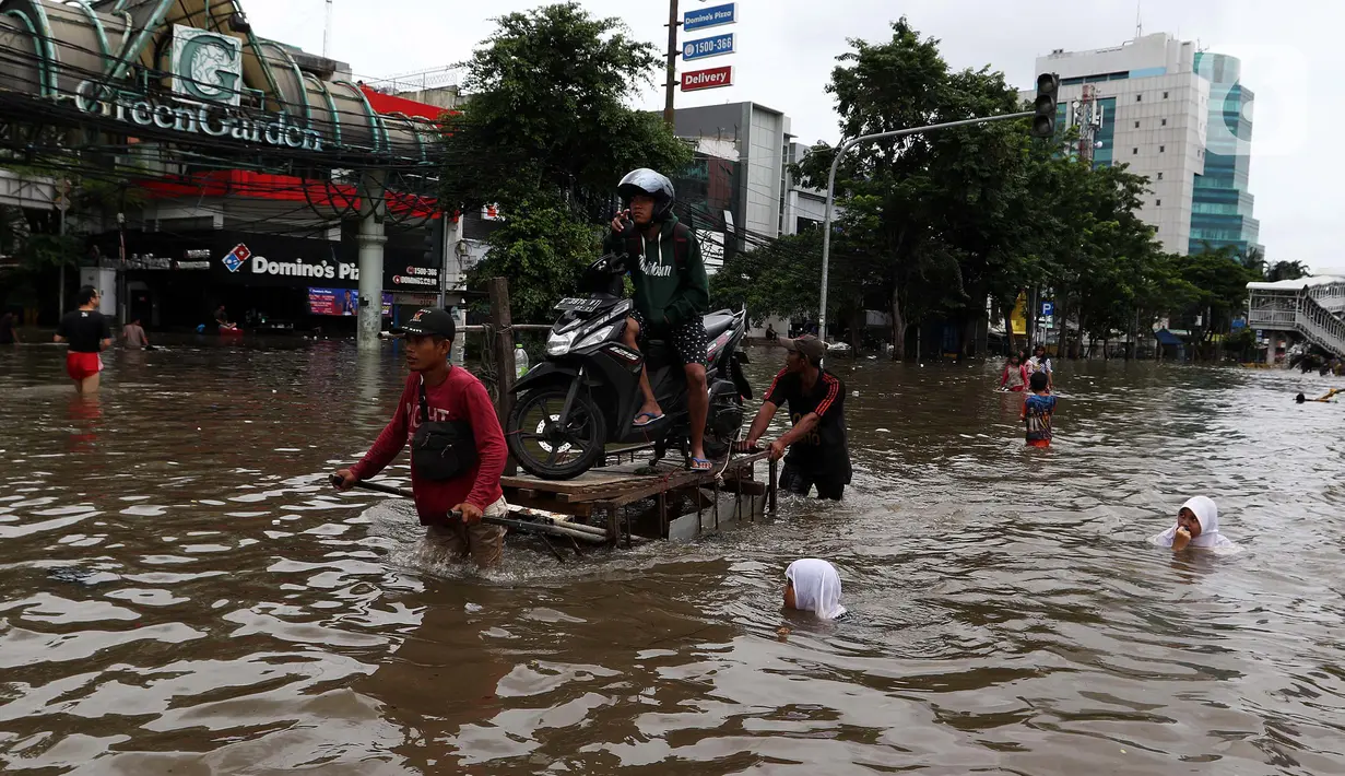 Pengendara sepeda motor menggunakan jasa angkut gerobak saat melintasi banjir di kawasan Green Garden, Jakarta Barat, Selasa (25/2/2020). Hujan yang mengguyur kawasan Jakarta membuat kawasan tersebut tergenang banjir setinggi 60-80 cm. (Liputan6.com/Johan Tallo)