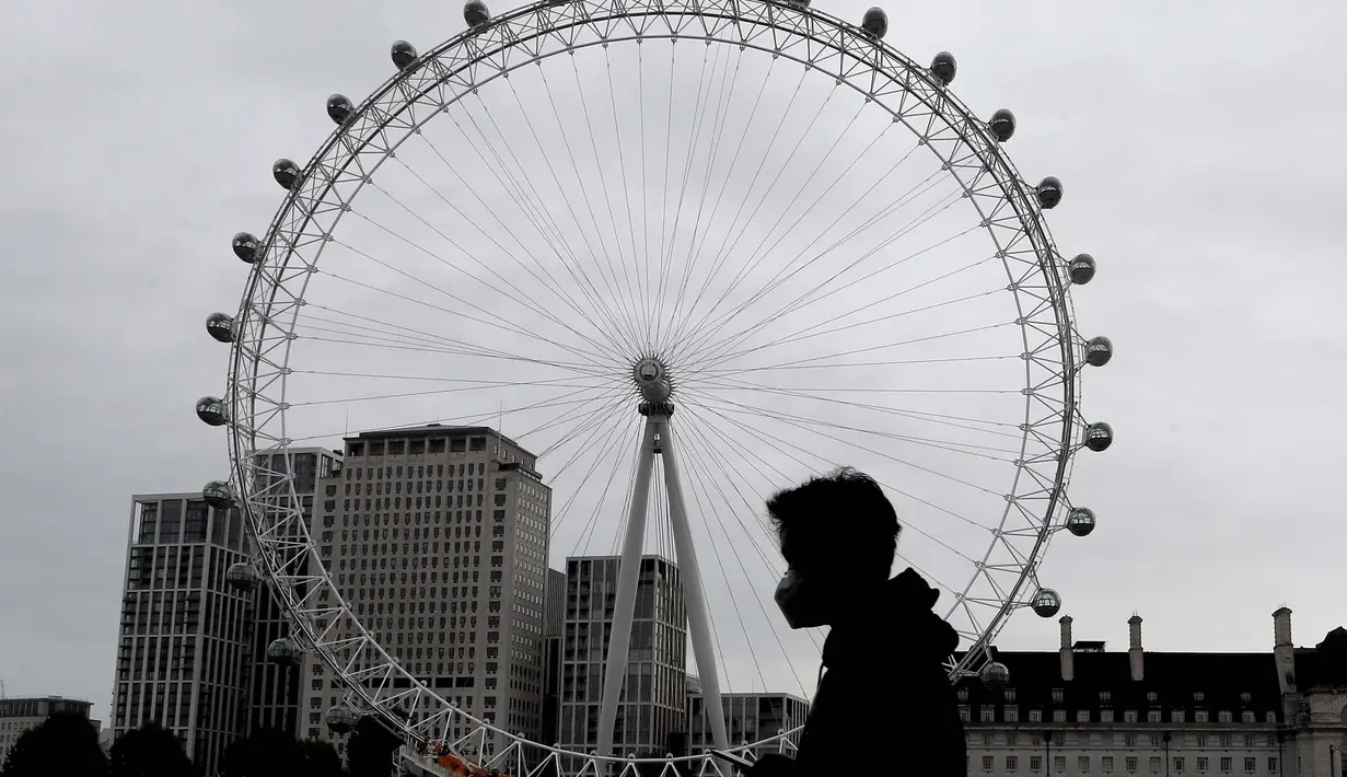Seorang pria memakai masker saat melewati London Eye di London, Kamis (29/10/2020). Sekitar 100.000 orang terjangkit virus corona setiap hari di Inggris, menurut studi terbaru Imperial College London. (AP Photo/Frank Augstein)
