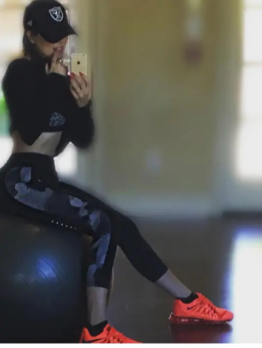 Berpose menggoda dengan satu jari di mulutnya, ia terlihat duduk di atas bola besar di depan dinding cermin. Dia mengenakan legging hitam dan atasan lengan panjang lalu bentuk perut yang rata. (viainstagram@khloekardashian/Bintang.com)