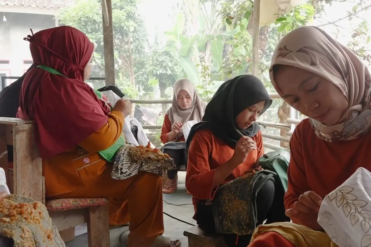 Perajin batik pewarna alami berbahan limbah kulit jengkol saat menggoreskan canting membuat motif khas budaya Lampung. (Liputan6.com/Ardi Munthe)