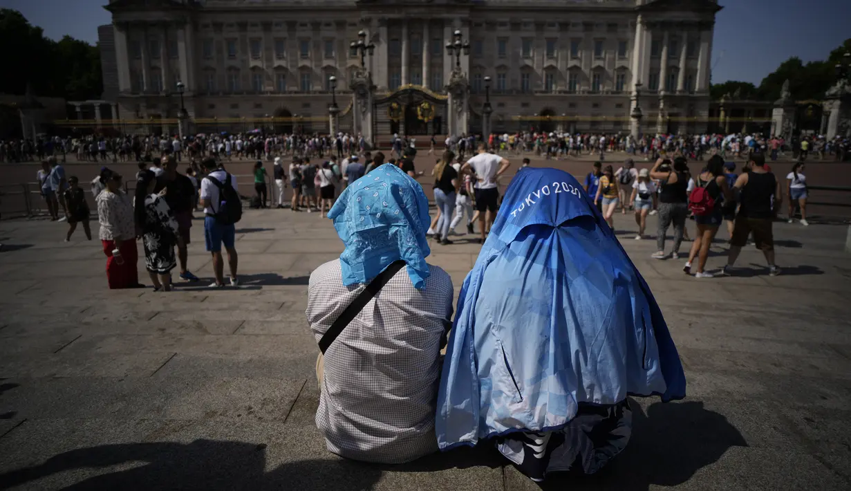 <p>Orang-orang duduk menutupi kepala mereka dari matahari setelah versi kecil dari upacara Pergantian Penjaga berlangsung di luar Istana Buckingham, selama cuaca panas di London, Senin (18/7/2022). Pemerintah Inggris telah mengeluarkan peringatan "merah" pertama mereka untuk panas ekstrem. (AP Photo/Matt Dunham)</p>