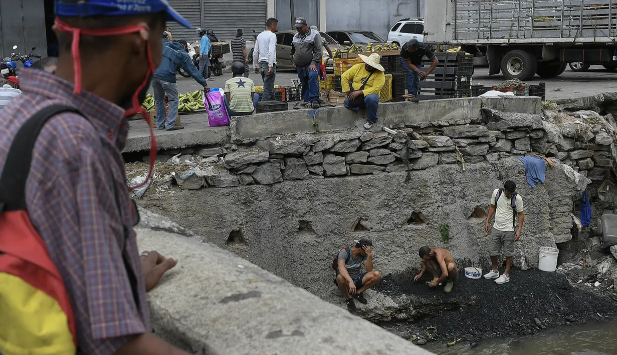 Pria mencari potongan tembaga, emas atau perak untuk dijual di tengah pandemi virus corona baru di Sungai Guaire yang tercemar, di lingkungan Quinta Crespo di Caracas, Venezuela (19/1/2021). Krisis ekonomi Venezuela telah mengirim jutaan orang melarikan diri. (AP Photo/Matias Delacroix)