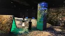 Seorang anggota staf dan anggota pers berdiri di instalasi digital interaktif bernama "Shifting Valley, Living Creatures of Flowers, Symbiotic Lives" selama pratinjau media "teamLab Forest" di gedung hiburan BOSS E・ZO FUKUOKA di Fukuoka, Jepang, Jumat (16/7/2021). (YUKI IWAMURA/AFP)