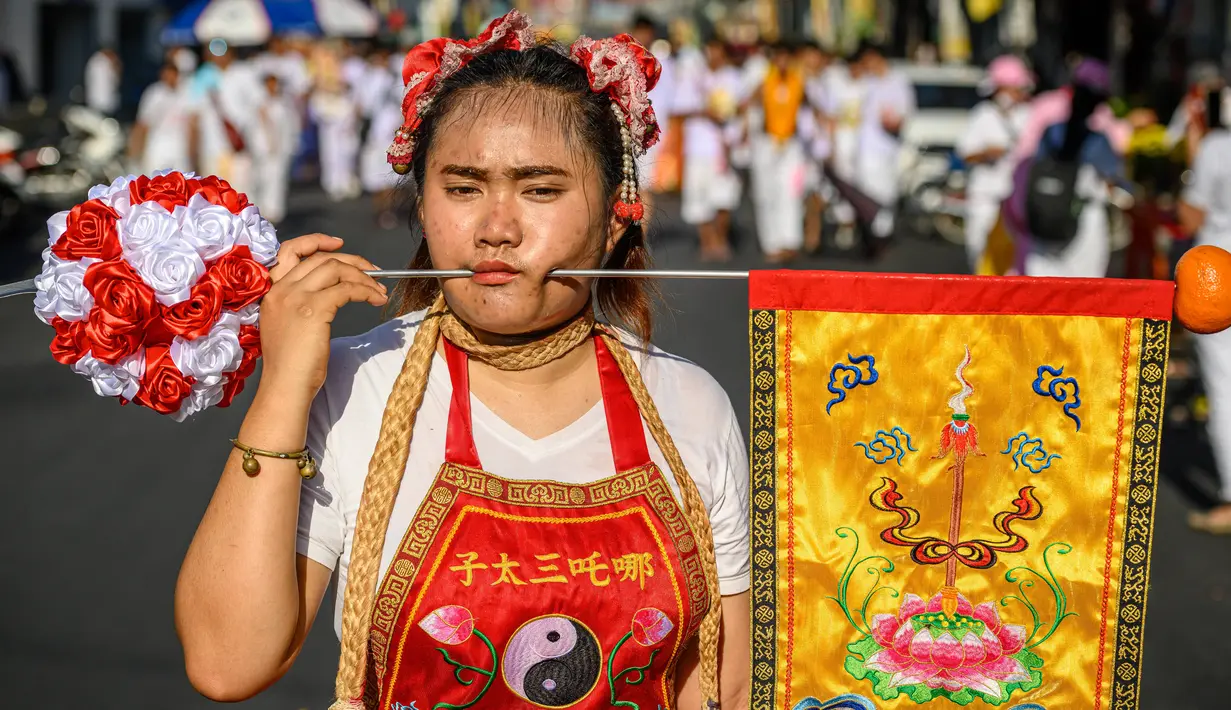 Seorang wanita menusuk pipinya dengan besi  saat mengikuti prosesi perayaan Festival Vegetarian tahunan di Phuket, Thailand, Kamis (3/10/2019). Festival ini biasanya berlangsung selama 9 hari di akhir September sampai Oktober. (AFP Photo/Mladen Antonov)