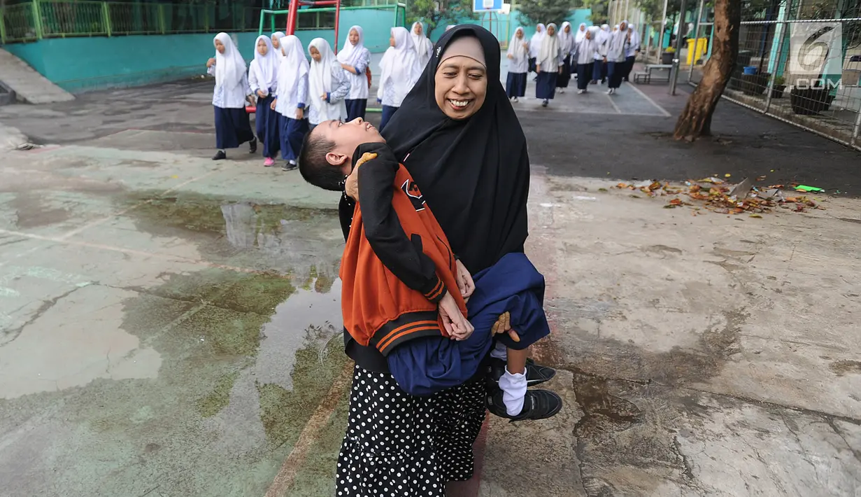 Fauzan Akmal Maulana (15), penderita Distrophia Muculor Progresive (DMP) atau penyakit otot lemah, digendong oleh ibunya, Winih Utami (49), saat bersekolah di SMP Terbuka 1 Tangerang Selatan, pada Jumat (22/3). (merdeka.com/Arie Basuki)