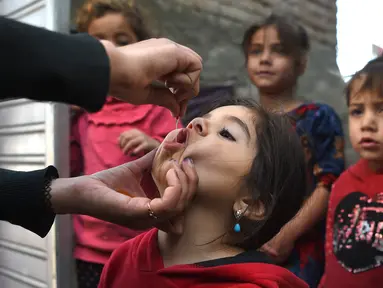 Tenaga kesehatan (kiri) memberikan vaksin polio kepada seorang anak selama kampanye vaksinasi di kawasan tua Kabul, Afghanistan pada 8 November 2021. Vaksinasi tersebut merupakan yang pertama sejak Taliban berkuasa di Afghanistan. (WAKIL KOHSAR / AFP)