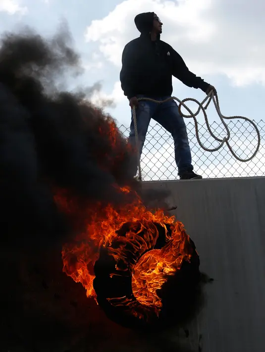 Seorang pengunjuk rasa membakar ban saat aksi di perbatasan Palestina-Israel, Ramallah, Jumat (17/2). Aksi tersebut untuk memperingati 12 tahun protes mereka atas tembok pemisah tersebut. (AP Photo / Majdi Mohammed)