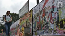 Warga berjalan di samping proyek revitalisasi Taman Ismail Marzuki (TIM) yang dipenuhi lukisan bentuk protes, Jakarta, Sabtu (29/2/2020). Kebijakan Pemprov DKI Jakarta merevitalisasi TIM dinilai cacat prosedural karena tidak pernah dibicarakan dengan seniman sebelumnya. (Liputan6.com/Johan Tallo)