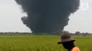 Petani beraktivitas dengan latar belakang akibat kebakaran Kilang Balongan di Indramayu, Jawa Barat, Senin (29/03/2021). Belum diketahui penyebab ledakan kilang Pertamina Balongan yang mengakibatkan kebakaran besar tersebut. (merdeka.com/Arie Basuki)