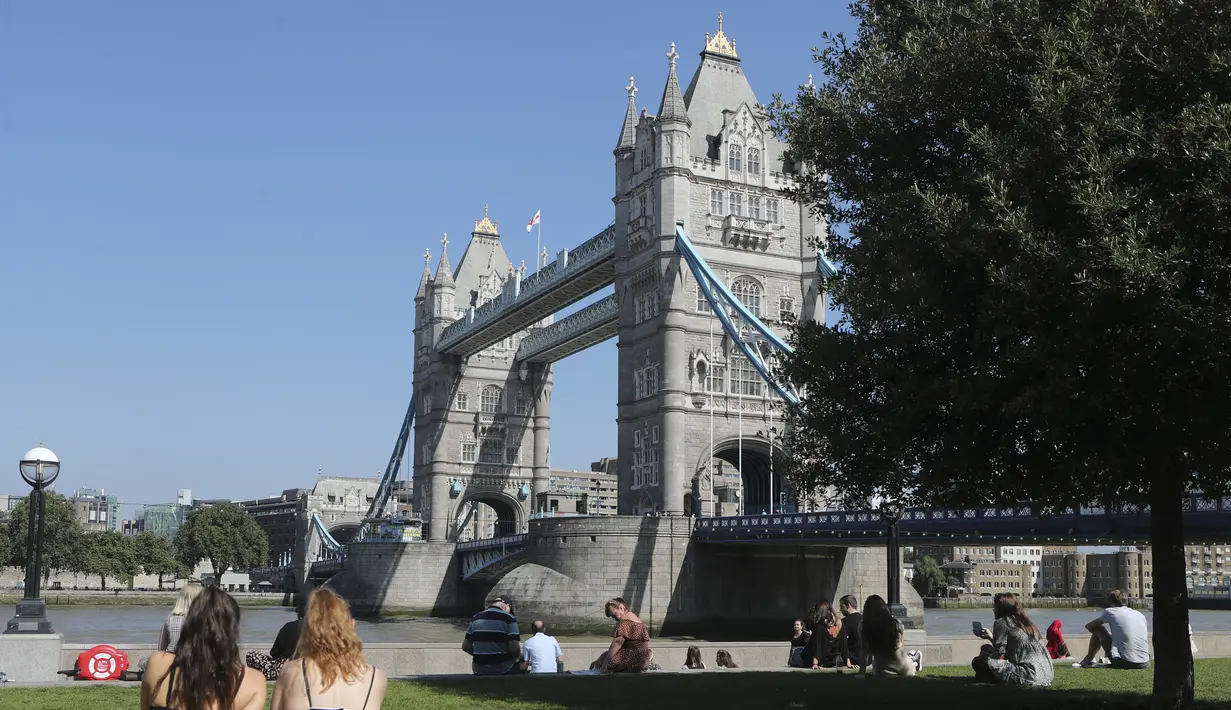 Dua wanita berjemur saat mereka duduk di rumput dekat Potters Field menghadap Tower Bridge saat suhu mendekati 30 derajat celsius di London, Selasa (7/9/2021).  (AP Photo/Tony Hicks)