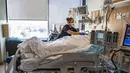 Petugas merawat pasien non-Covid-19 di dalam satu ruangan di samping kamar pasien Covid-19, di bangsal ICU UMass Memorial Medical Center di Worcester, Massachusetts, Selasa (4/1/2022). Rumah sakit mengklaim mereka dipenuhi pasien dan tidak memiliki banyak tempat tidur tersisa. (Joseph Prezioso/AFP)