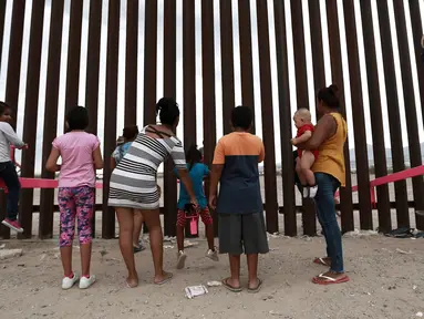 Anak-anak bermain jungkat-jungkit yang dipasang di antara pagar pemisah Meksiko dengan Amerika Serikat, Ciudad de Juarez, Meksiko, Minggu (28/7/2019). Jungkat-jungkit tersebut dirancang seorang profesor arsitektur California, Ronald Rael. (AP Photo/Christian Chavez)