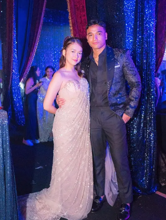 <p>Kali ini keduanya mengenakan outfit pesta. Fadly dengan kemeja hitam yang serasi dengan celana panjangnya, ditumpuk dengan blazer yang juga berwarna hitam berkilauan. Sedangkan Rebecca mengenakan off-the-shoulder dress bernuansa emas, dengan detail bagian dada berbentuk hati. Foto: Instagram.</p>