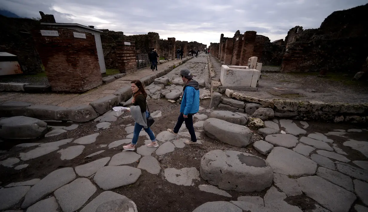 Wisatawan menyeberangi Via di Nola yang berbatu, Pompeii, Italia, Senin (25/11/2019). Kota Pompeii ditemukan 1.500 tahun setelah letusan gunung berapi Vesuvius yang tragis. (Filippo MONTEFORTE/AFP)