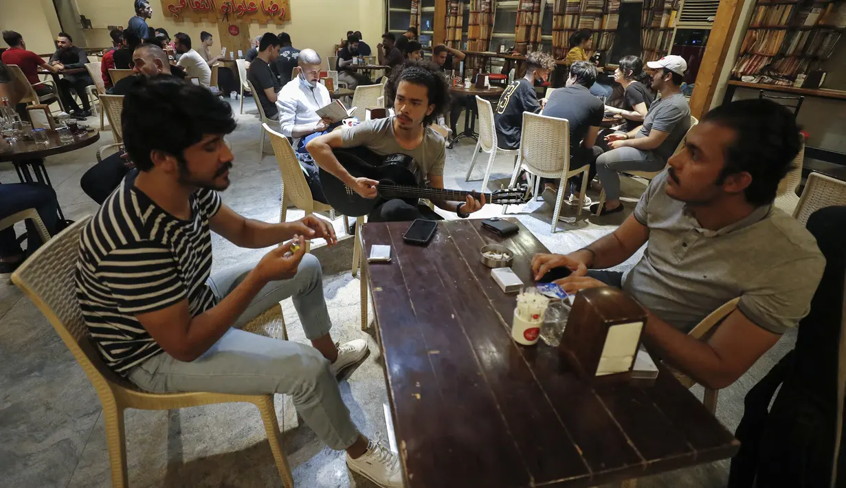 Mohammed (23) bermain gitar saat duduk bersama teman-temannya di sebuah kedai kopi di Distrik Karrada, Baghdad, Irak, 6 Agustus 2021. Banyak pemuda Irak di Baghdad berusaha untuk menjadi modern, bahkan ketika mereka mengakui negaranya mungkin tidak memiliki masa depan. (AHMAD AL-RUBAYE/AFP)