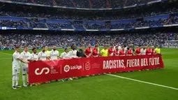 Sejumlah pemain Real Madrid membentangkan banner yang bertuliskan "Rasis, di luar sepak bola" pada laga lanjutan Liga Spanyol 2022/2023 antara Real Madrid melawan Rayo Vallecano pada Kamis (25/05/2023) dini hari WIB. Los Blancos memberikan aksi solidaritas sebelum laga tersebut setelah Vinicius Jr menjadi korban rasisme pada Minggu (21/05/2023) lalu. (AP Photo/Manu Fernandez)