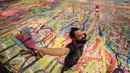 Seniman Inggris Sacha Jafri berpose di atas lukisannya yang berjudul "The Journey of Humanity" di Dubai, Uni Emirat Arab pada 1 Oktober 2020. Lukisan yang berukuran dua lapangan sepak bola ini merupakan bagian dari proyek amal “Humanity Inspired”. (AP Photo/Kamran Jebreili)